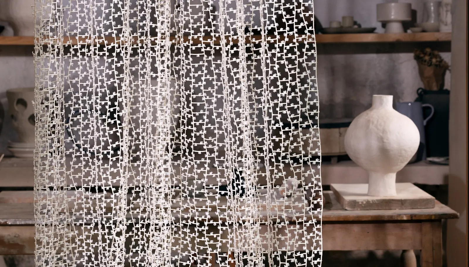 Sheer lace-patterned curtain in front of a shelf of ceramic vases