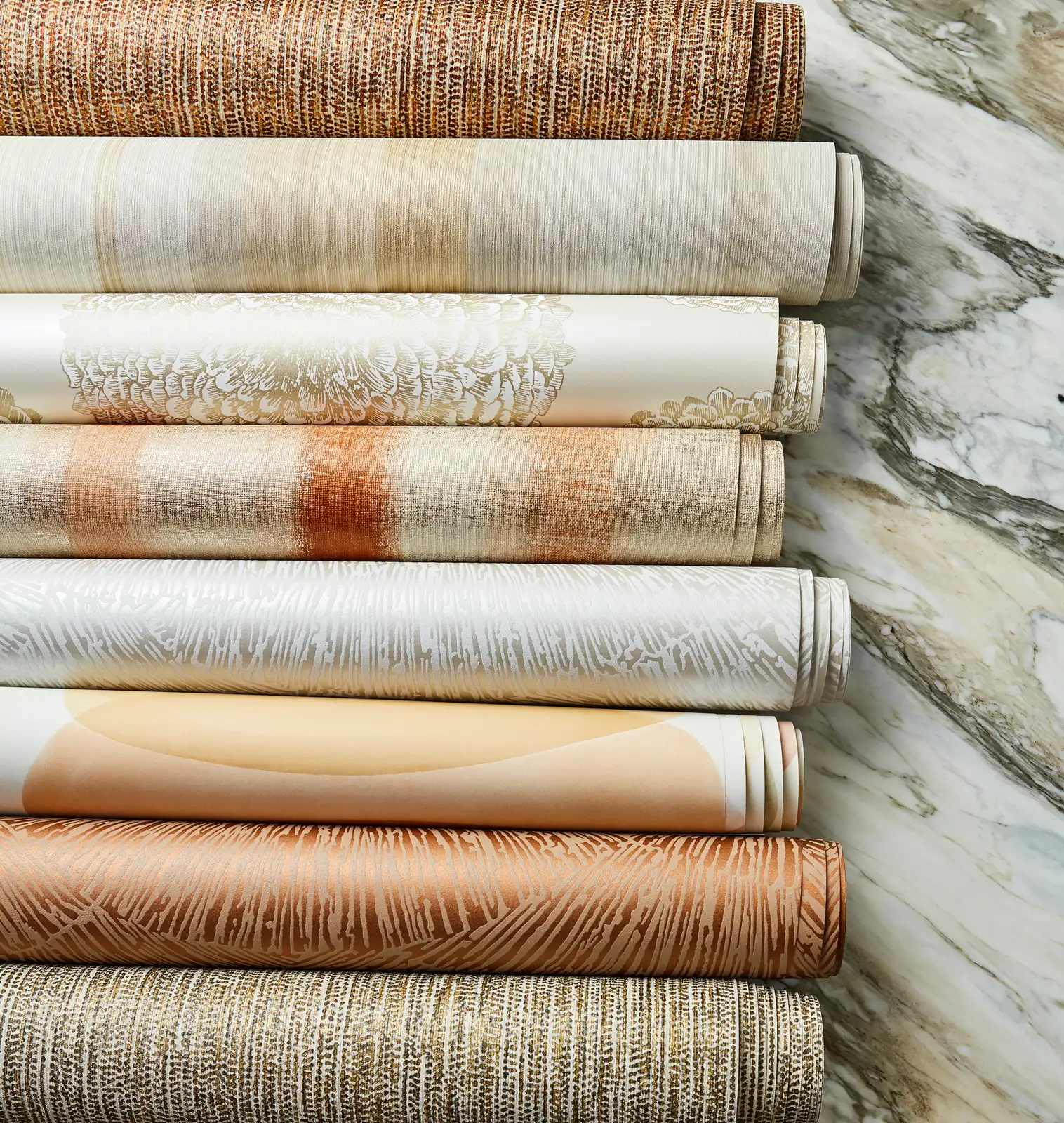 Stack of rolled wallcoverings in cream, ochre and rust beside marble
